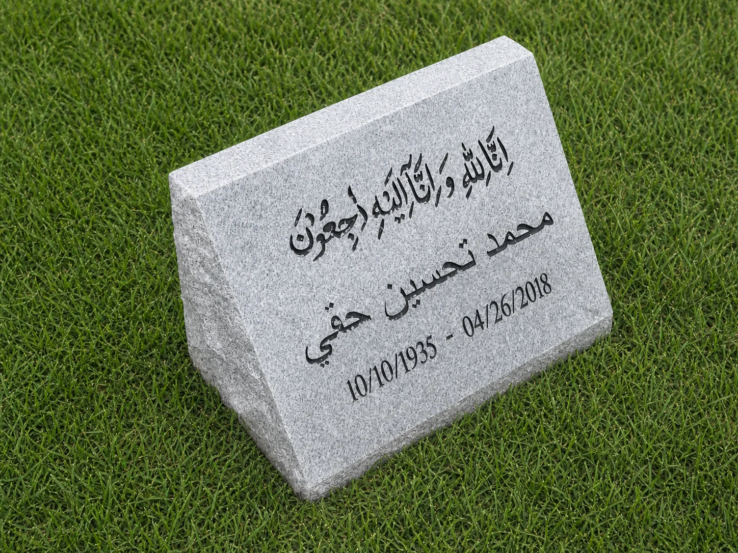 Light gray granite slanted marker with Arabic inscription on grass